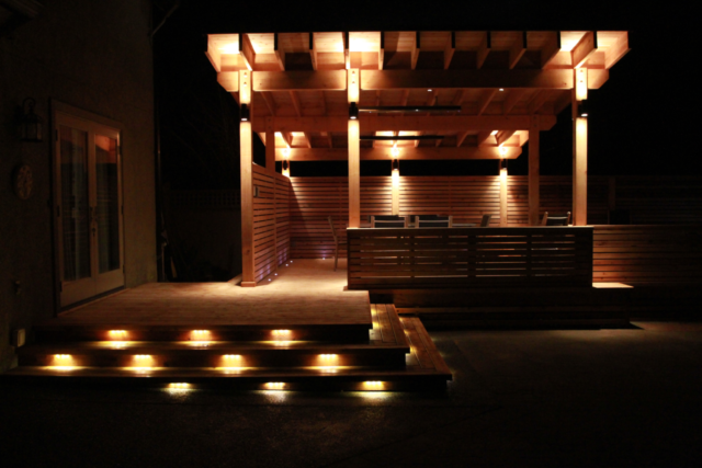 Wood patio lit up at night with landscape lighting
