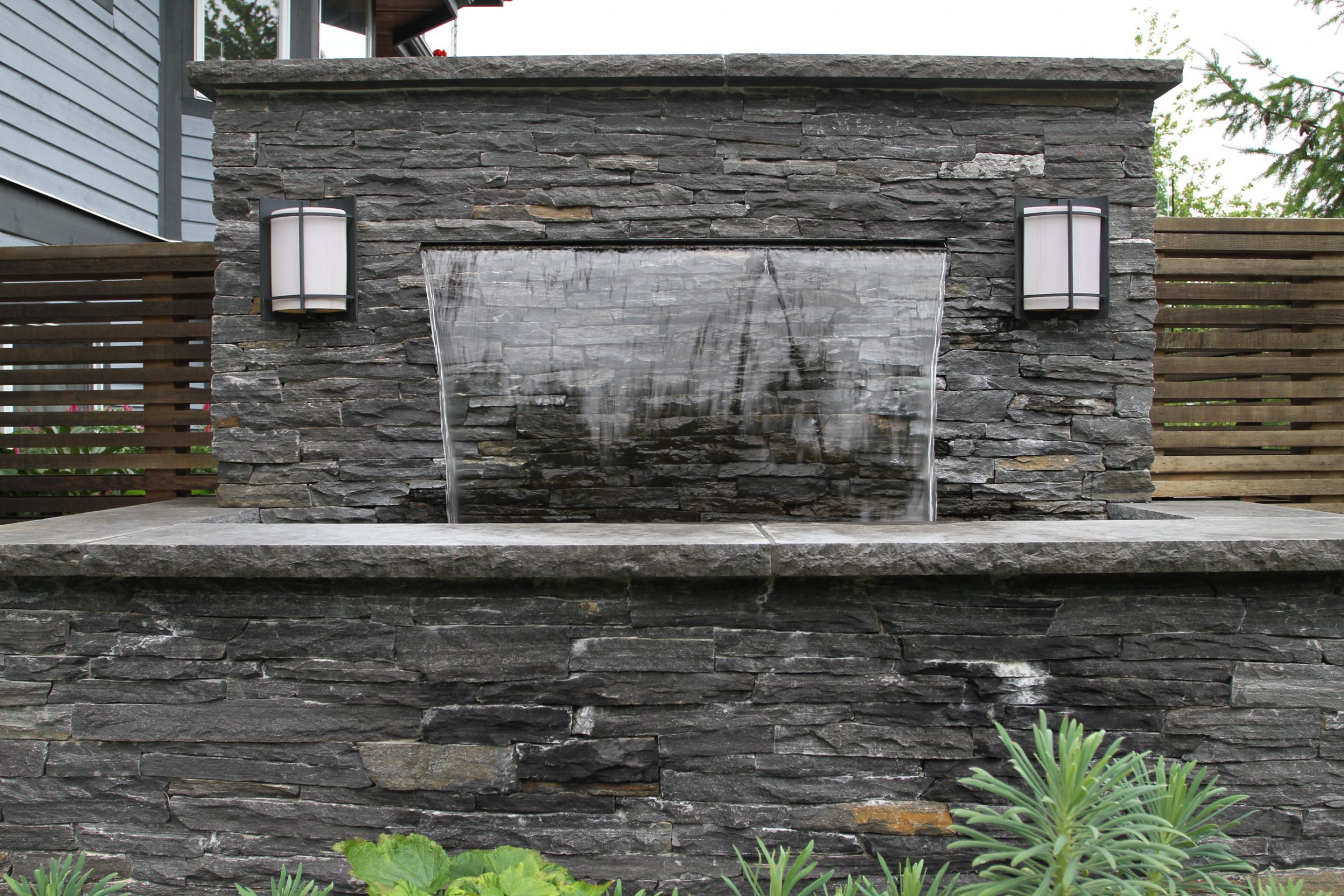 Modern stone wall waterfall with outdoor sconces