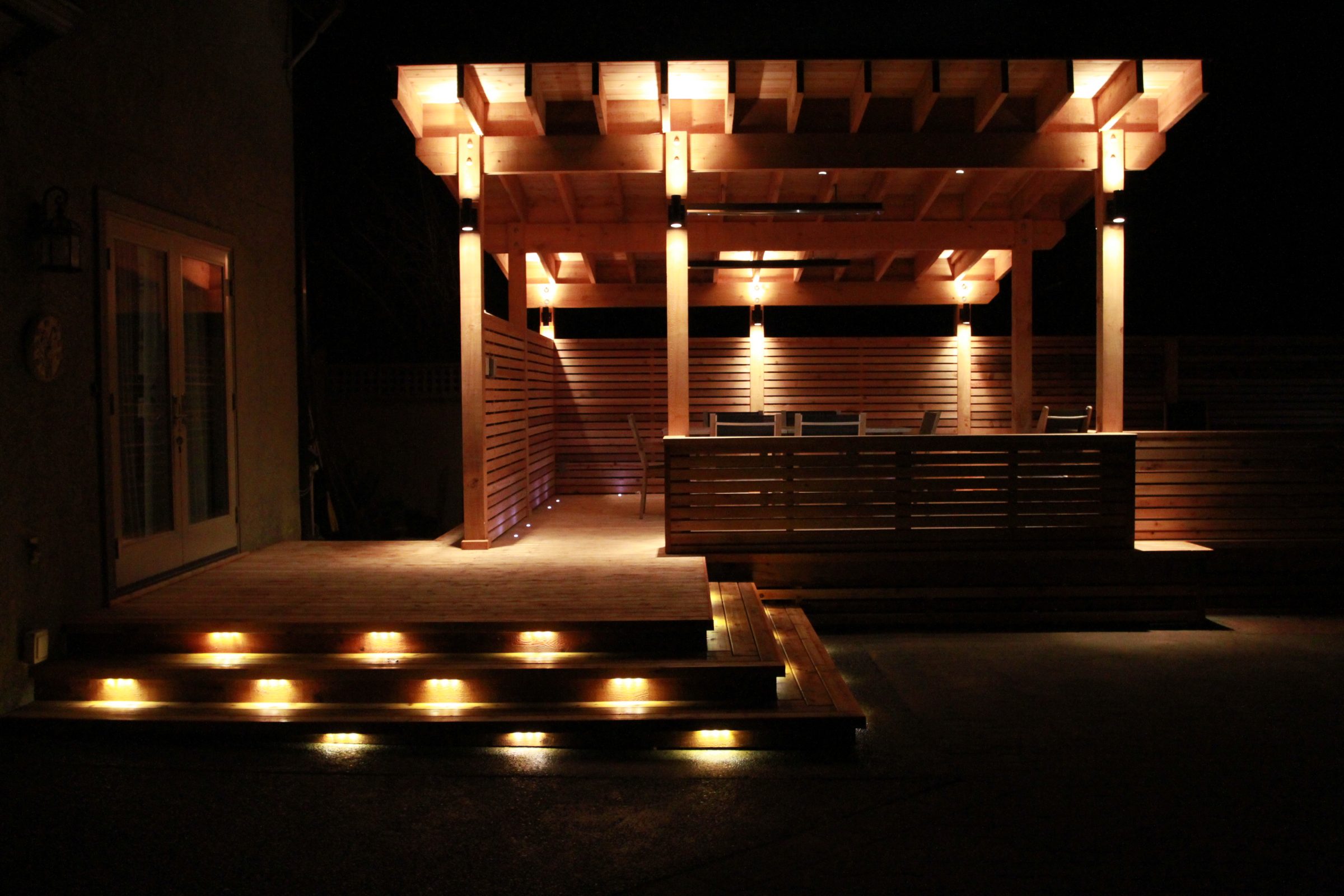 Warmly lit wooden patio with pergola at night