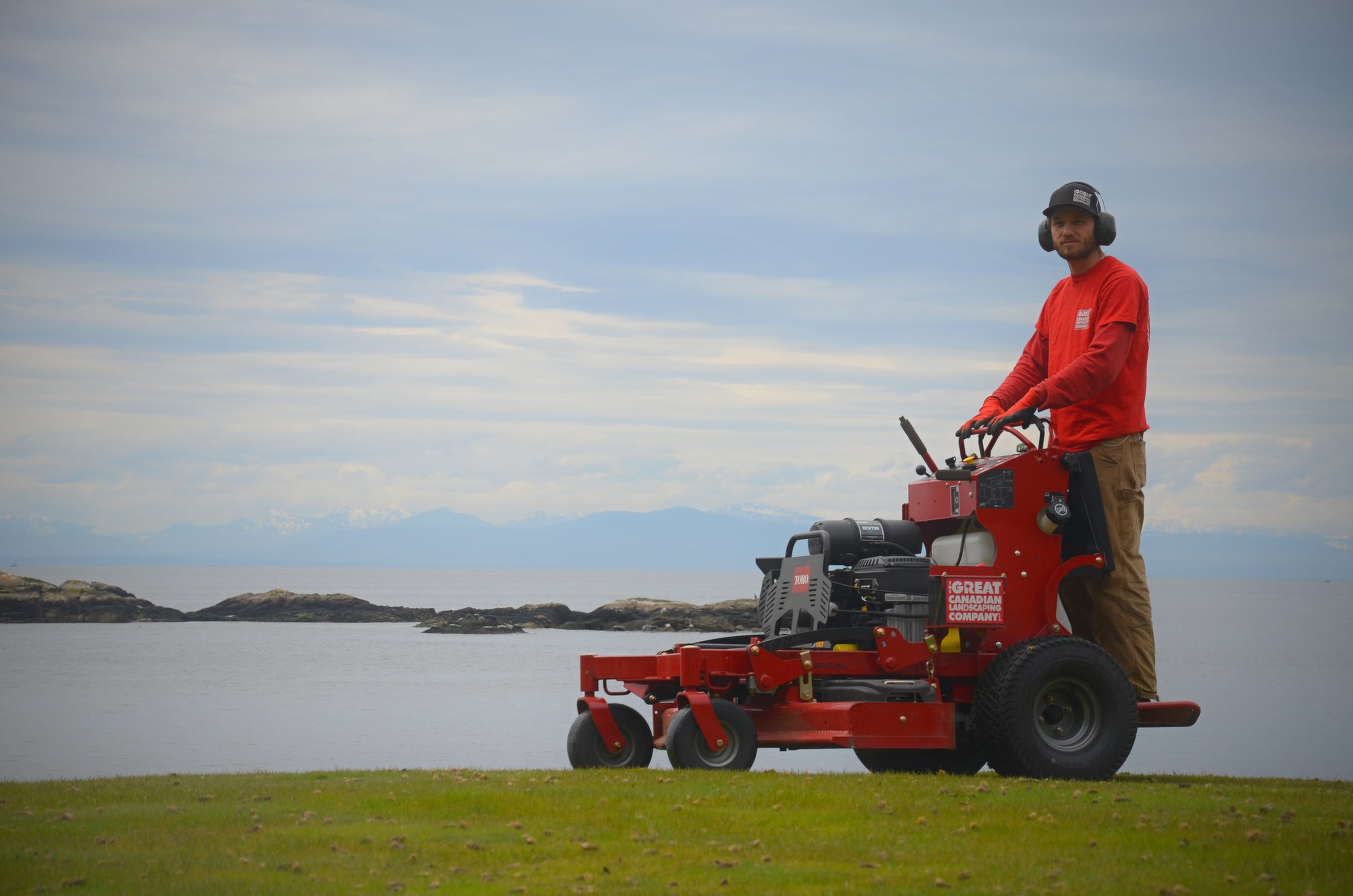 Landscaper operating red mower by waterfront