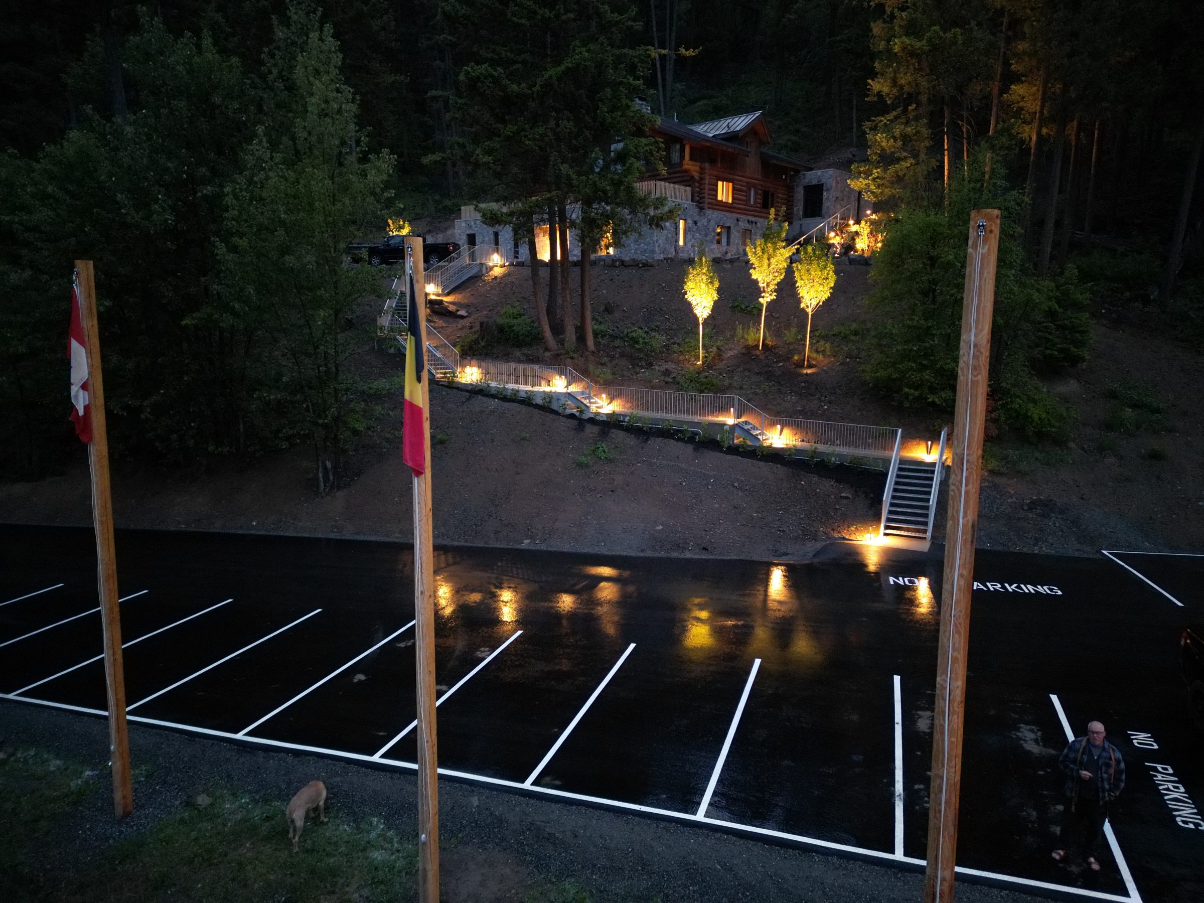 Illuminated hillside cabin above wet parking lot at night