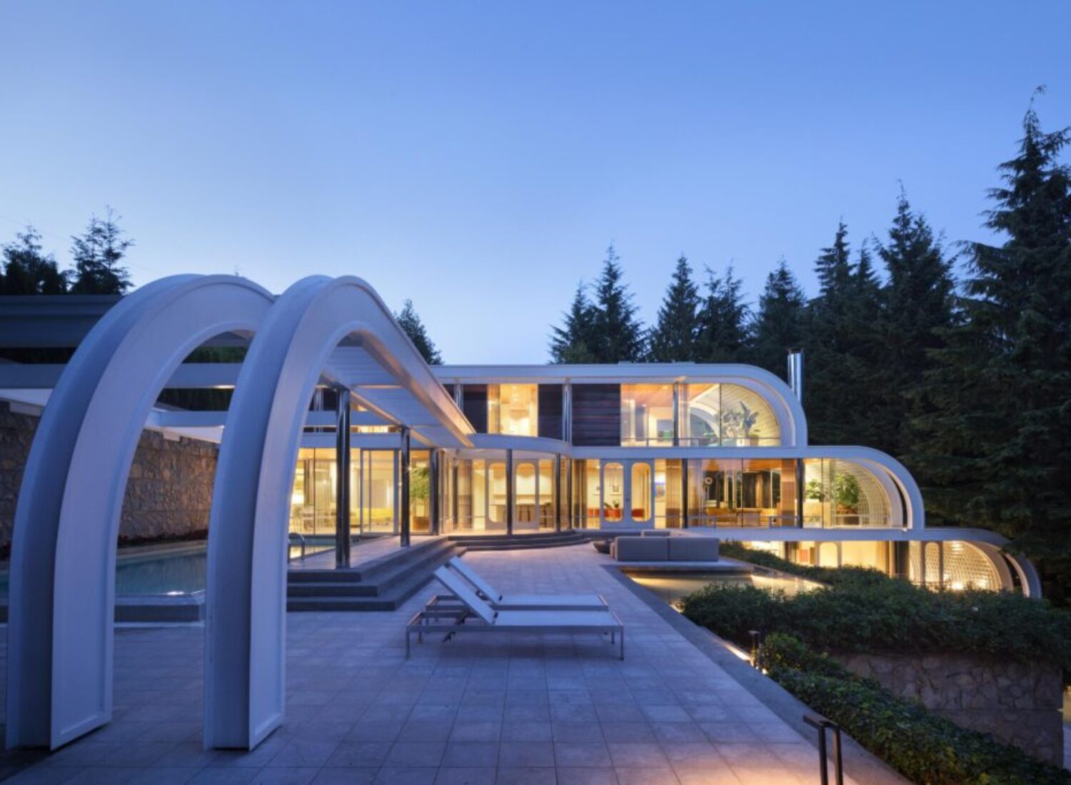 Modern curved glass home with pool at dusk