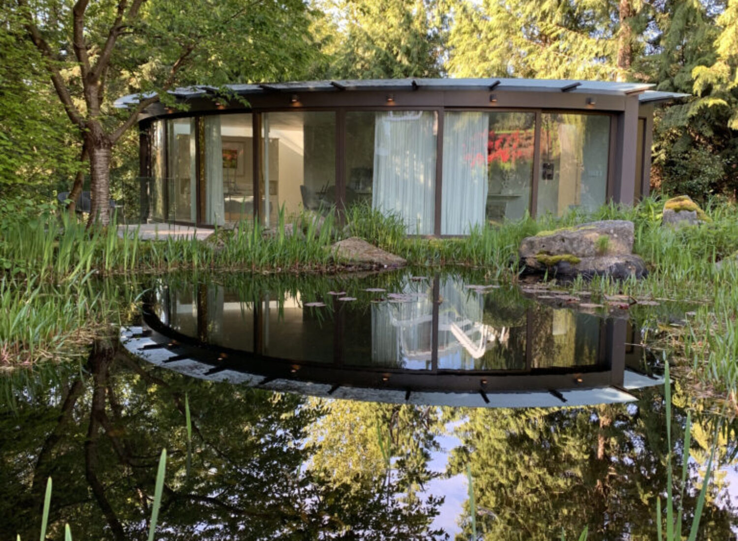 Modern circular glass house reflected in pond