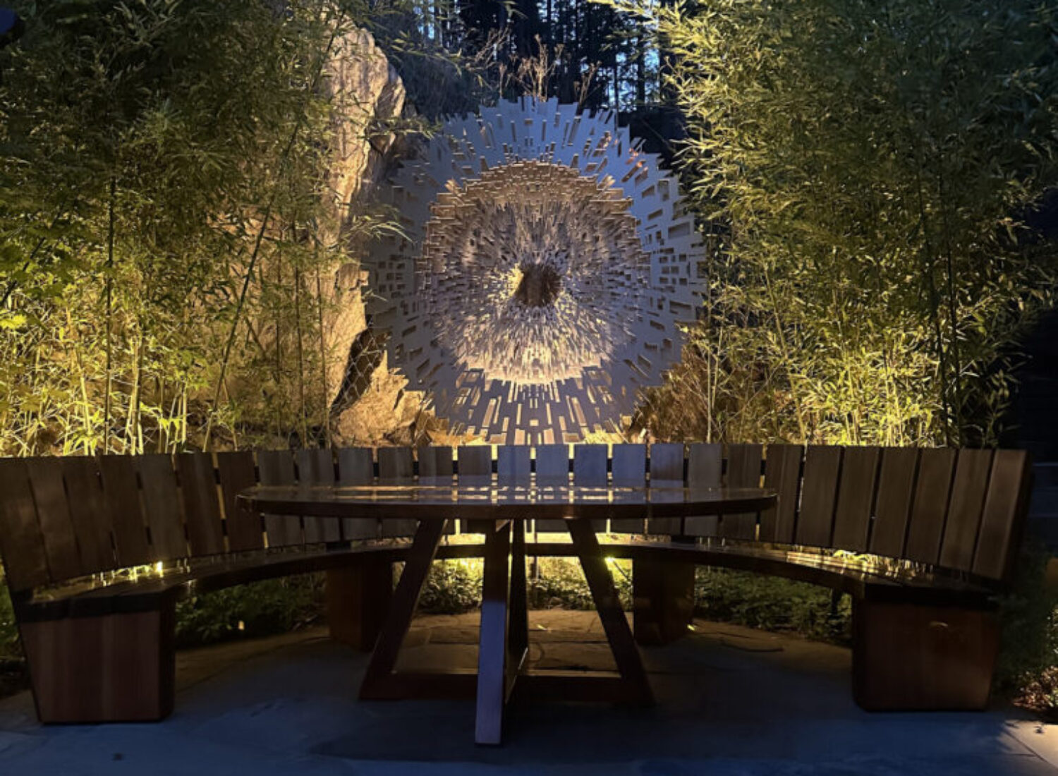 Circular wooden bench facing illuminated garden sculpture