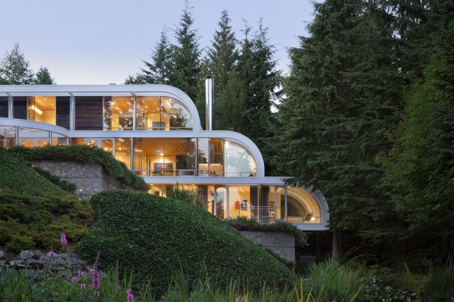 Modern glass house on forested hillside at dusk