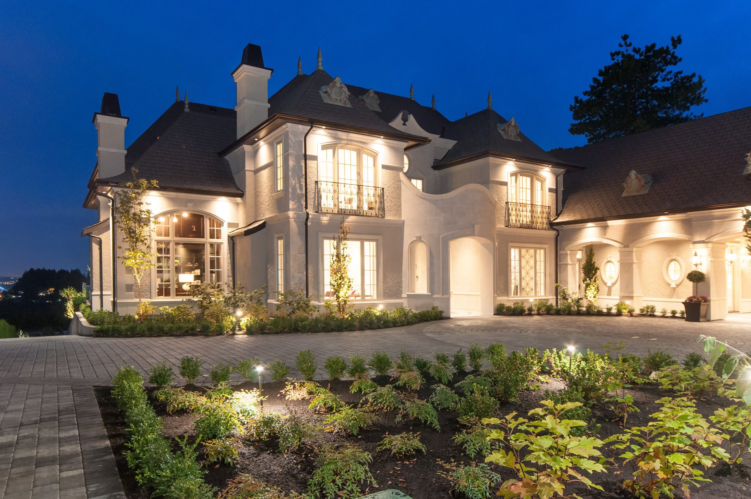 Luxury mansion illuminated at dusk with landscaped garden