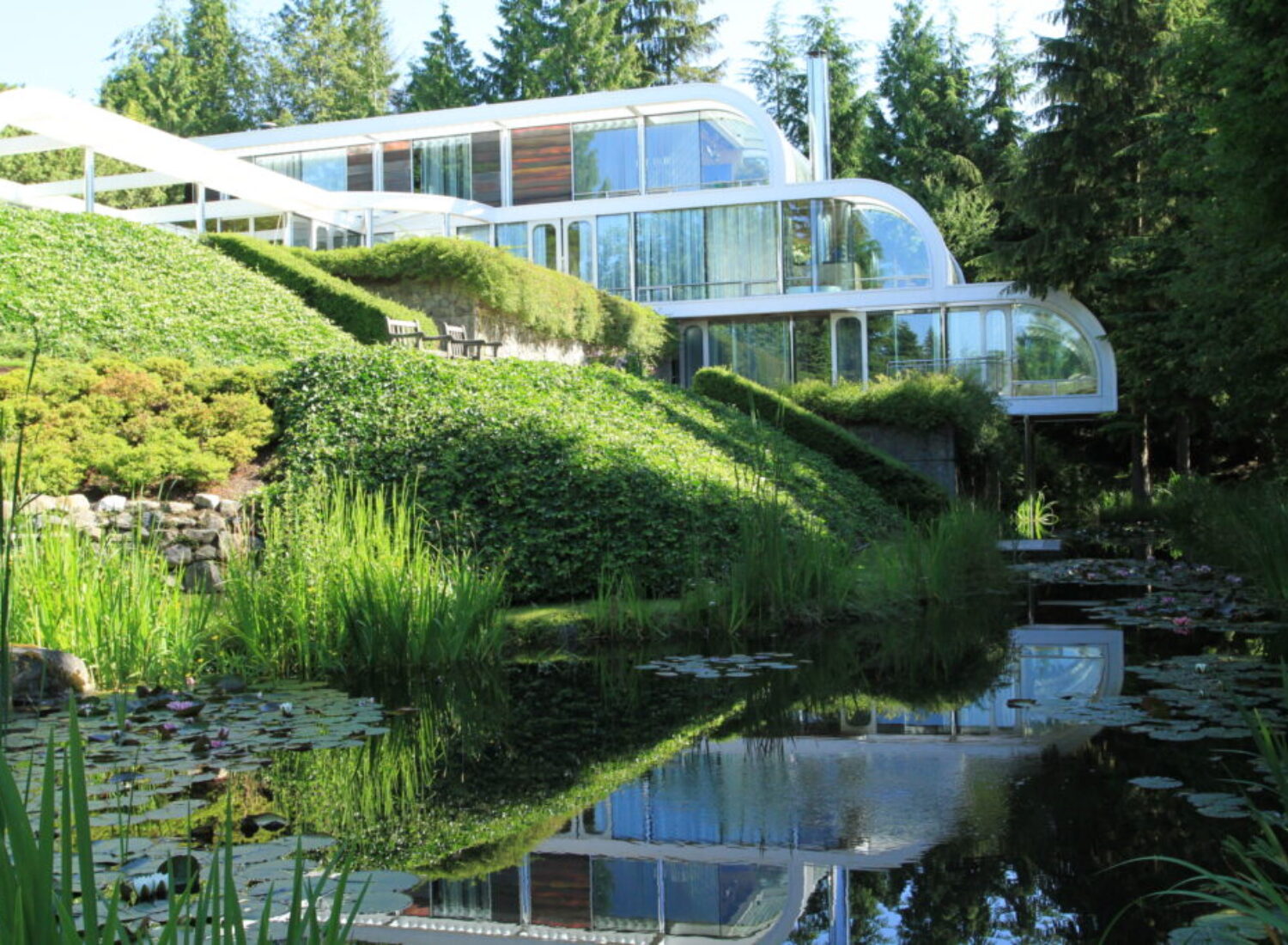 Modern glass house overlooking lush pond and gardens