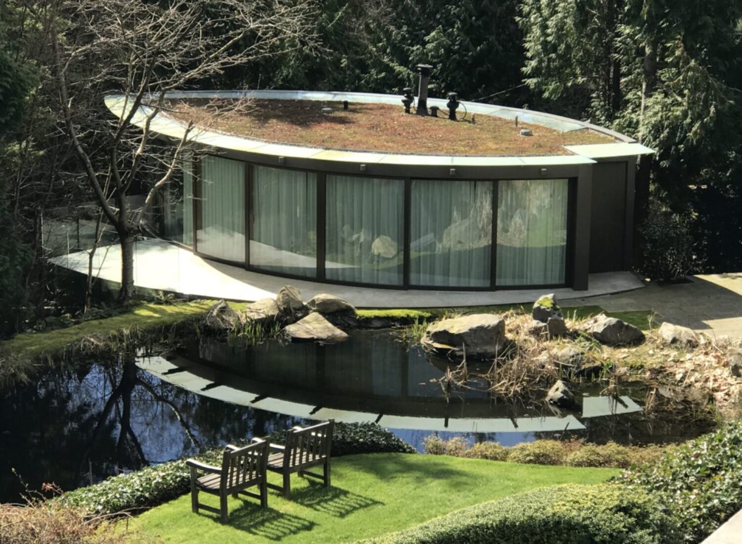 Modern circular glass house beside tranquil pond