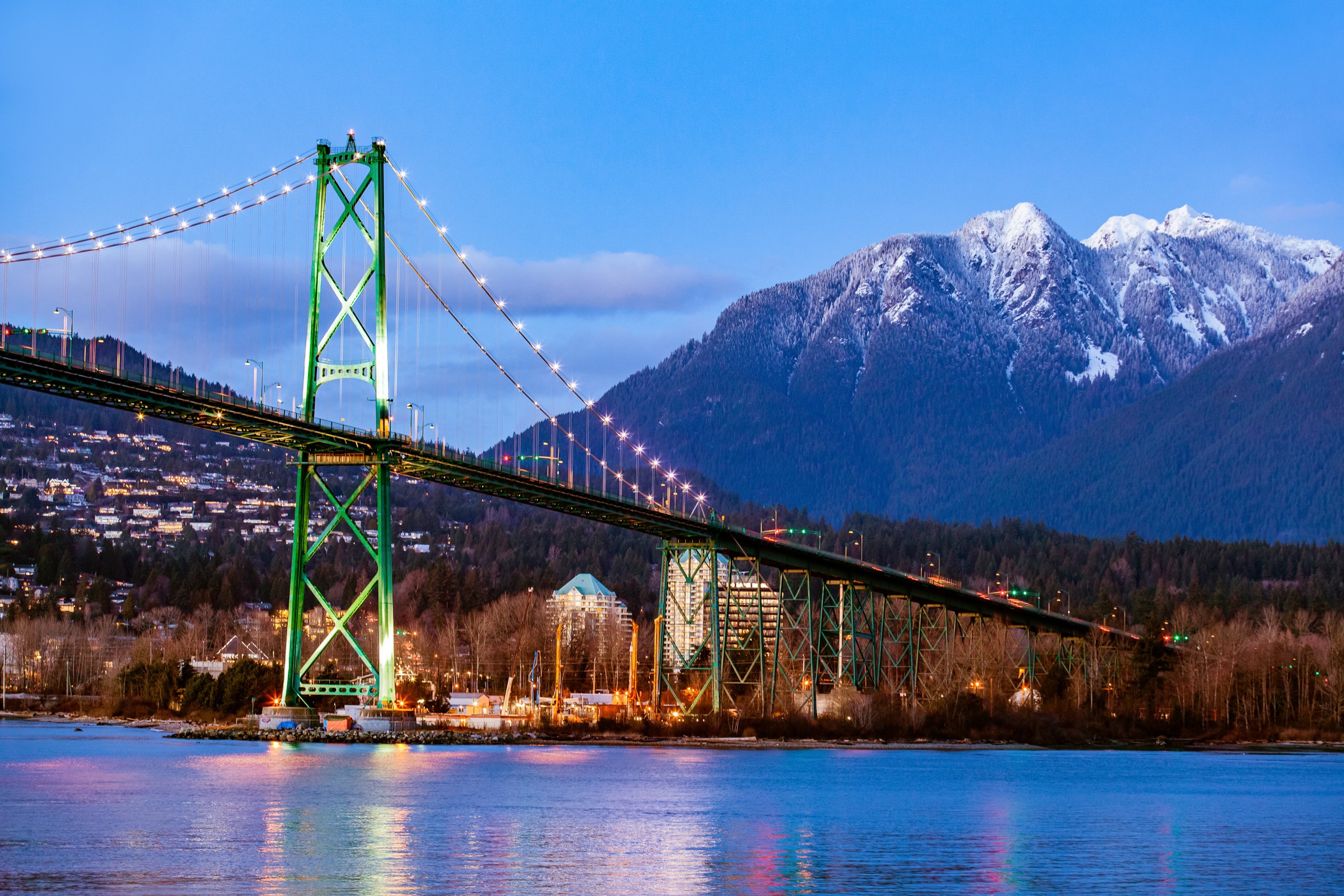Suspension bridge at dusk with snowy mountains