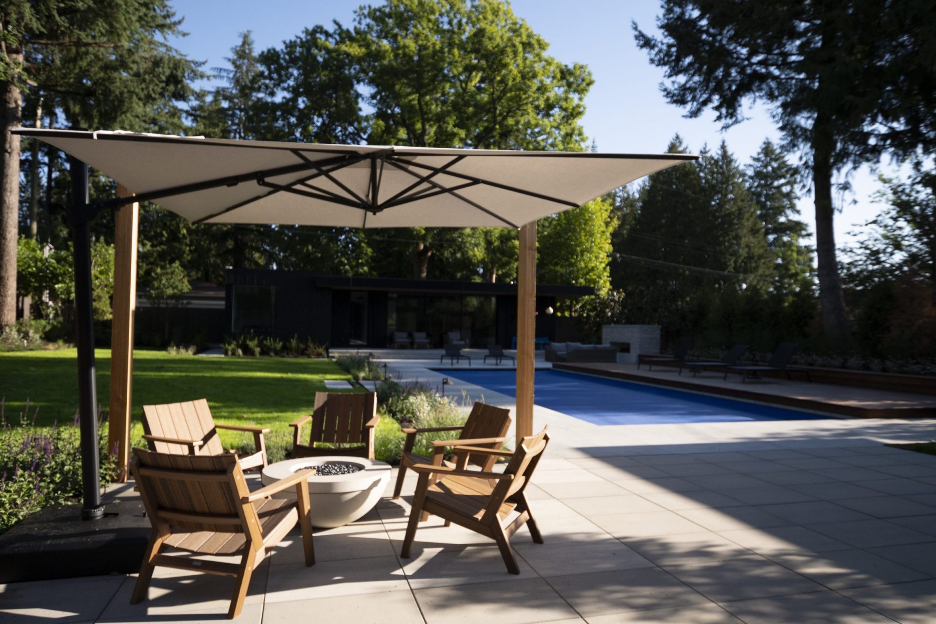 Modern paver patio with a gas fire bowl seating area, large cantilever umbrella, and outdoor swimming pool.